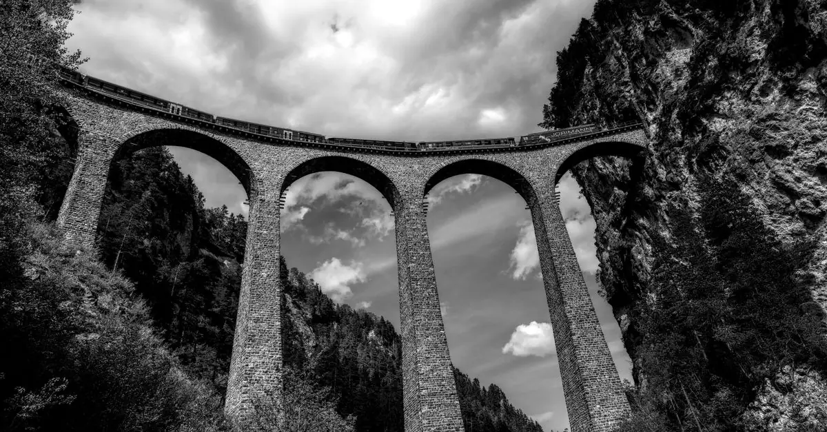 Black and white view of the iconic Landwasser Viaduct with a train passing, nestled in the Swiss Alps.
