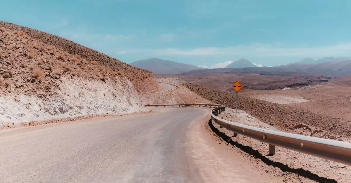 A winding deserted road in the Antofagasta desert, showcasing the barren landscape under a clear blue sky.