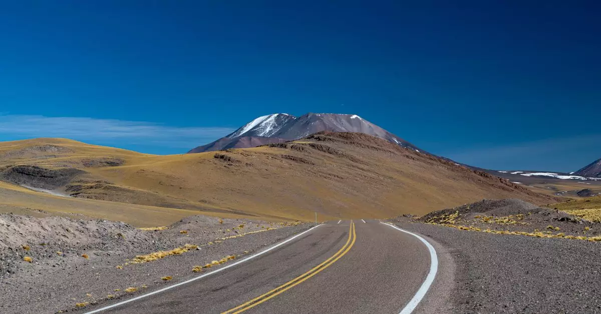 A winding road leading to a snow-capped mountain under a clear blue sky.