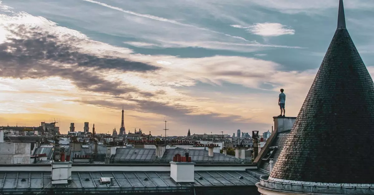 A mesmerizing view of Paris rooftops and the Eiffel Tower at sunset, with a person standing atop a building.