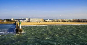 Vibrant seaside view of Calais, France with pier, sandy beach, and cityscape.