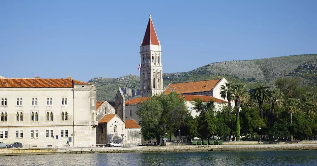 Scenic view of Trogir waterfront with the bell tower of St. Lawrence Cathedral against a mountainous backdrop.