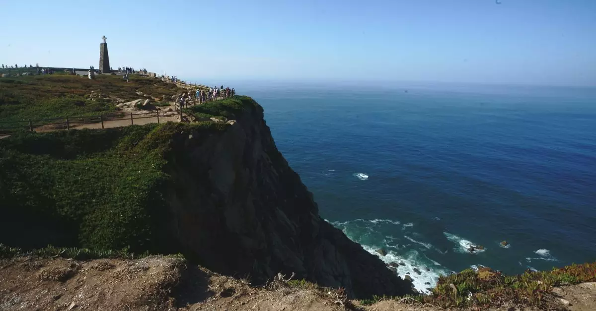 A breathtaking view of a coastal cliff with a lighthouse, set under a clear blue sky.