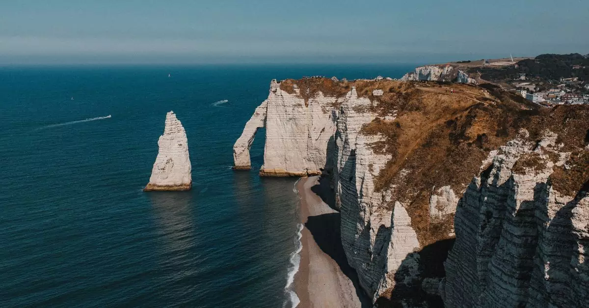 Stunning aerial view of Etretat's white chalk cliffs meeting the blue sea under clear skies in Normandy, France.