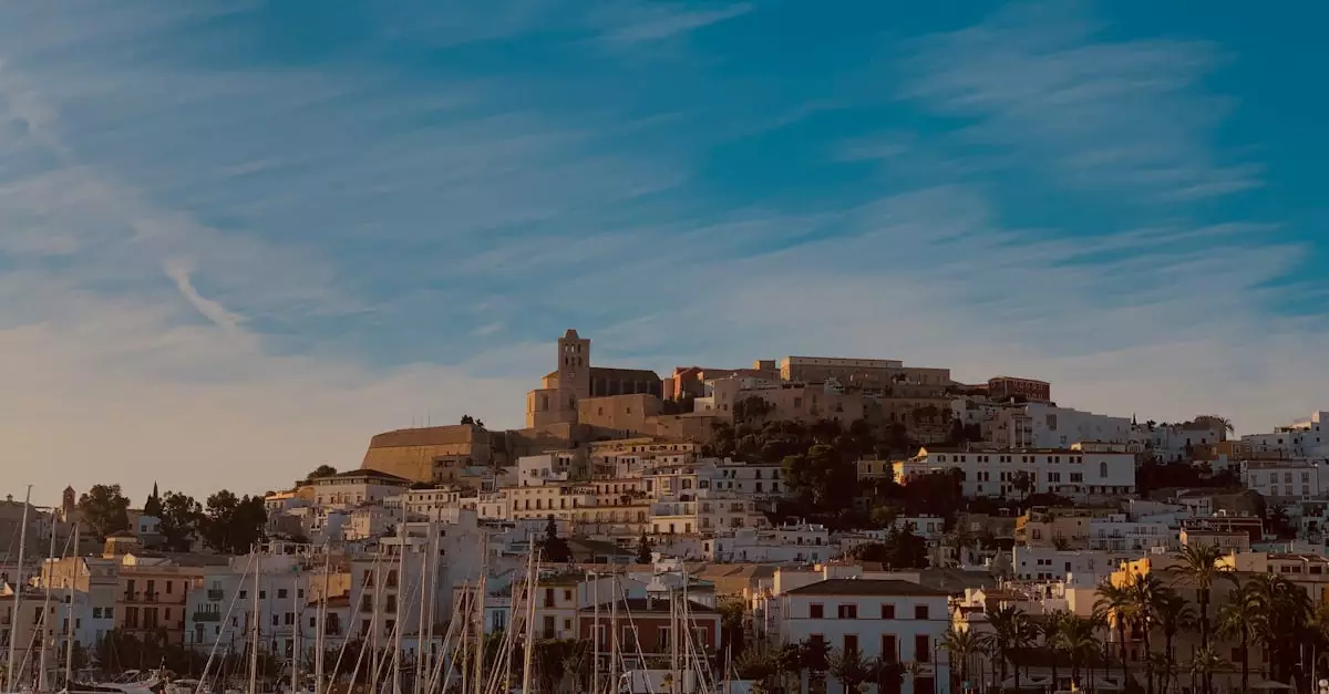 A tranquil view of Ibiza harbor with sailboats and historic buildings at dusk.