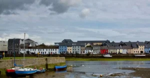 Charming row of colorful houses along waterside in Galway, Ireland, under a cloudy sky.