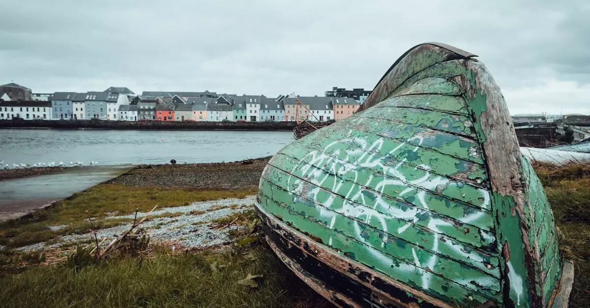 Old boat on Galway Bay shore with colorful houses in the background.