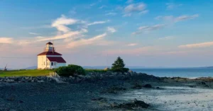 Picturesque Gilberts Cove lighthouse with rocky shore in Nova Scotia at sunset.
