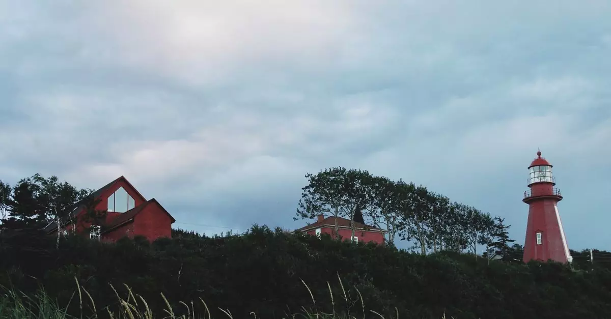 A scenic view of a red lighthouse and cottages amidst greenery under a blue sky in Quebec City.