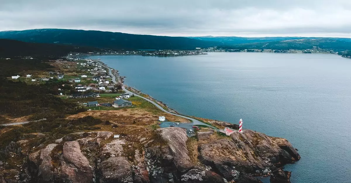 Drone view of beacon near road and dwelling houses on mountain near sea under cloudy sky
