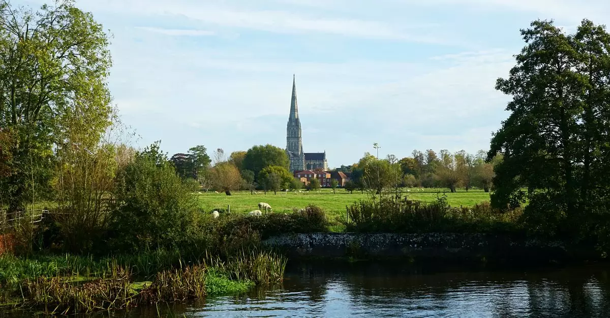 Salisbury Cathedral's iconic spire seen from a tranquil rural landscape in England.