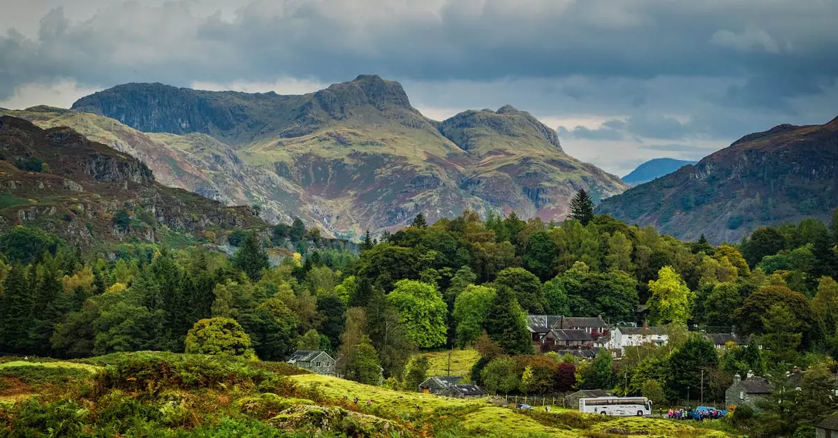 Scenic view of a tranquil village nestled among lush green trees and majestic mountains under a cloudy sky.