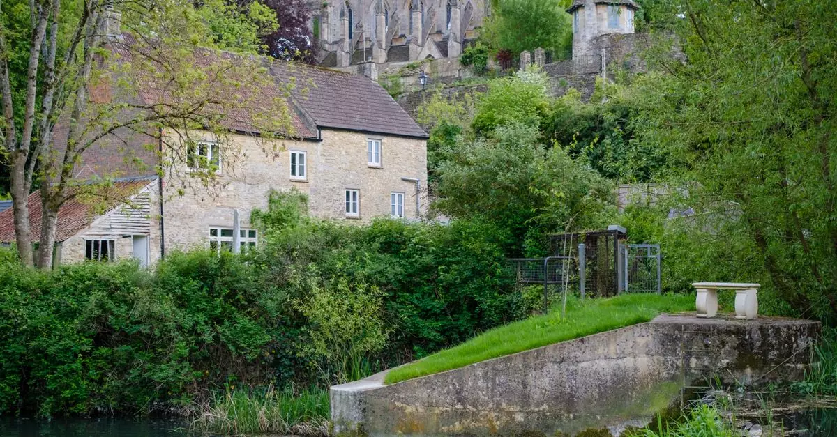 Tranquil riverside scene with historical architecture and lush greenery in Malmesbury, England.