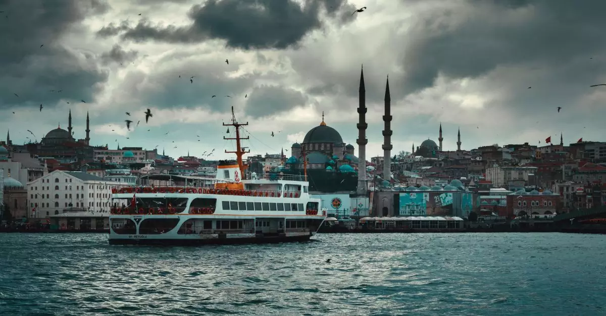 Modern cruise ship floating on rippling river near famous New Valide Sultan Mosque against cloudy sky in Istanbul