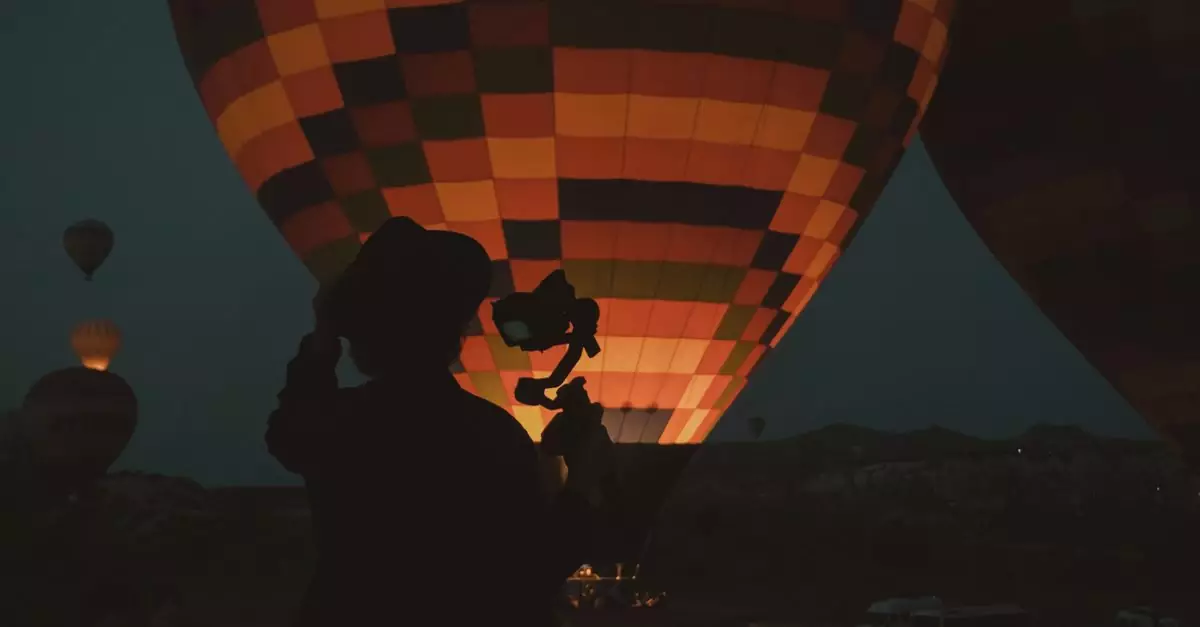 Silhouette of a photographer capturing illuminated hot air balloons at night in Türkiye.