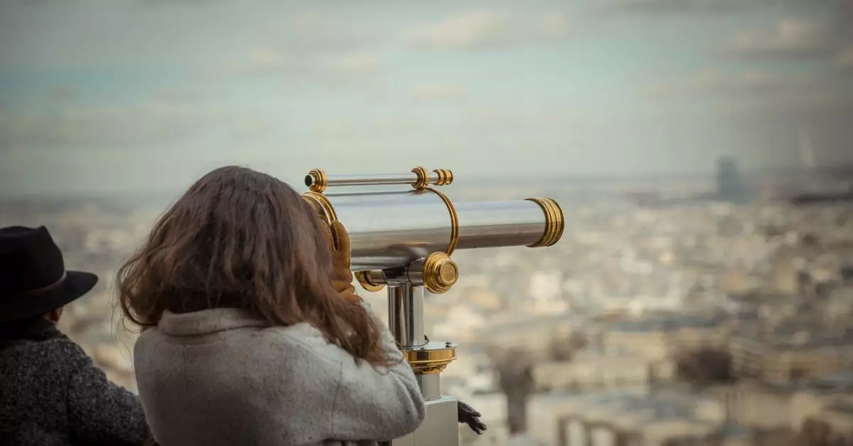A woman uses a telescope to observe a sprawling cityscape during the day.