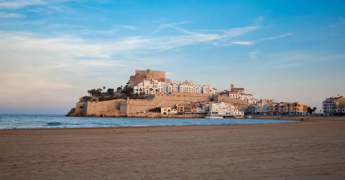 Serene landscape featuring Pe&ntilde;&iacute;scola Castle with a vast sandy beach and blue sky.