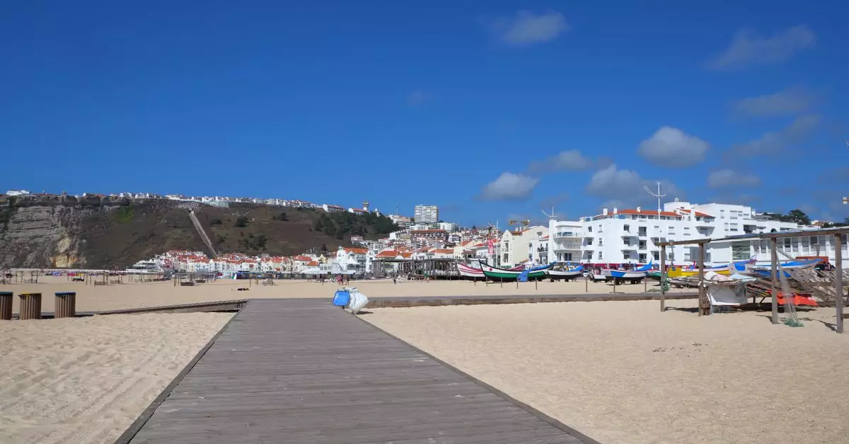 Explore the beautiful beachside view of Nazar&eacute;, Portugal, featuring traditional boats and a bright blue sky.