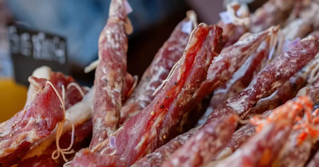 Assorted gourmet cured meats on display at a bustling market stall for food enthusiasts.