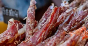 Assorted gourmet cured meats on display at a bustling market stall for food enthusiasts.
