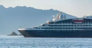A sleek black cruise ship sails past majestic mountains on a clear day.