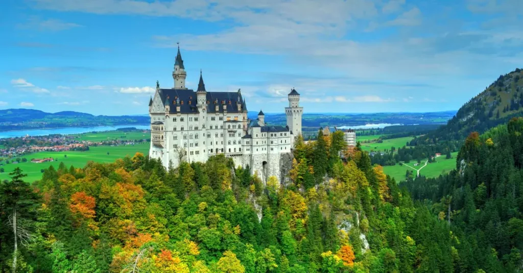 Aerial view of Neuschwanstein Castle amid vibrant autumn foliage with scenic landscape.