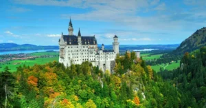 Aerial view of Neuschwanstein Castle amid vibrant autumn foliage with scenic landscape.