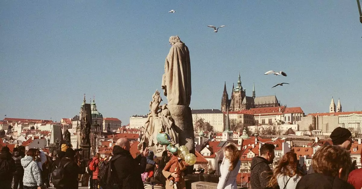 Bustling scene on Charles Bridge, Prague, with tourists and St. Vitus Cathedral in the background.