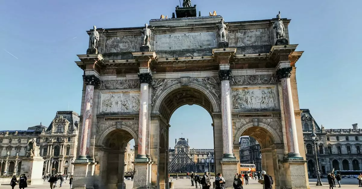 From below of aged Arc de Triomphe du Carrousel with statues on pavement with anonymous travelers in Paris