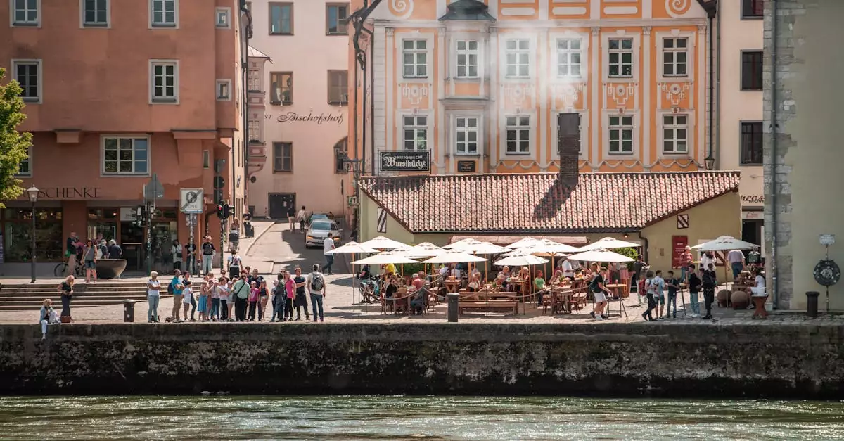 Busy riverside caf&eacute; in historic Regensburg, bustling with people under sunny umbrellas.