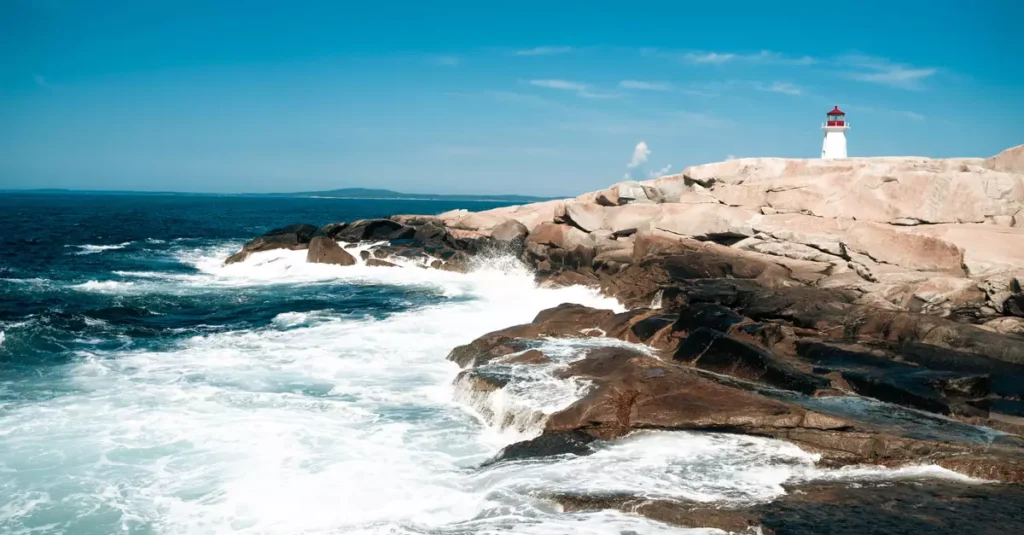 Dramatic landscape of Peggys Cove Lighthouse with crashing waves on a sunny day.