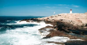 Dramatic landscape of Peggys Cove Lighthouse with crashing waves on a sunny day.