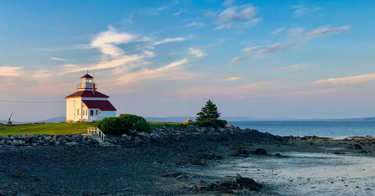 Picturesque Gilberts Cove lighthouse with rocky shore in Nova Scotia at sunset.