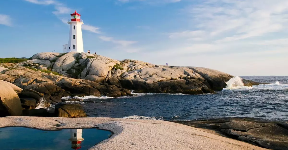 Lighthouse on rocky coast with ocean waves and bright sky, perfect for maritime themes.
