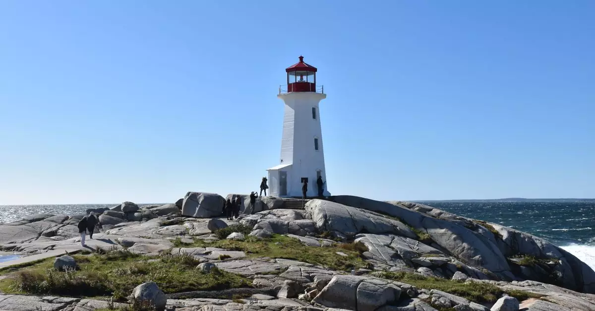 A stunning day view of the iconic Peggy's Cove Lighthouse surrounded by rocky terrain and ocean waves.
