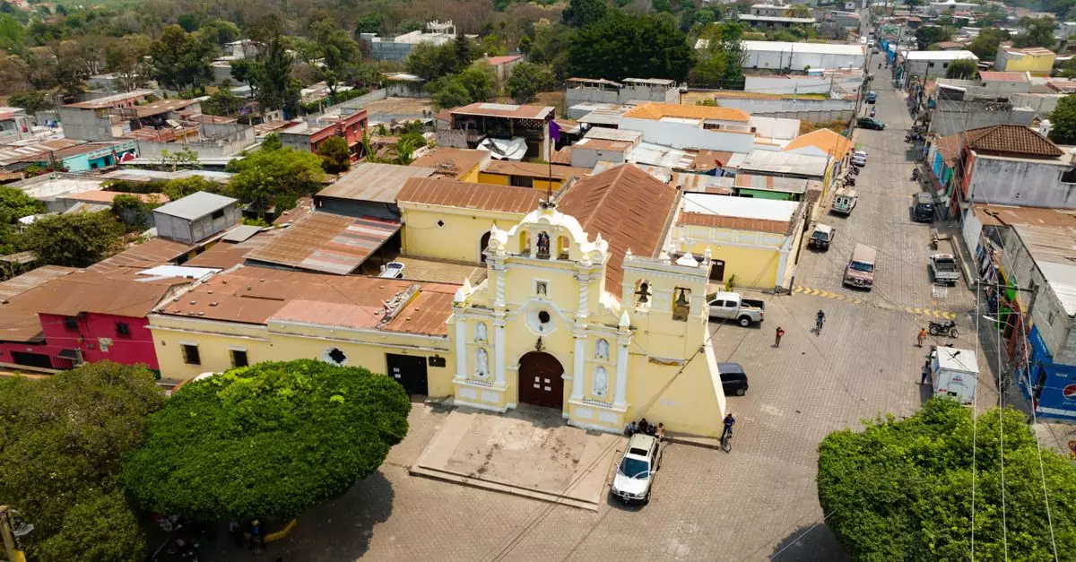 Captivating aerial view of a historic church in a vibrant Guatemalan town, showcasing colorful buildings.