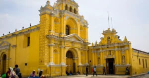 A vibrant yellow church in Guatemala City with local people and architecture.