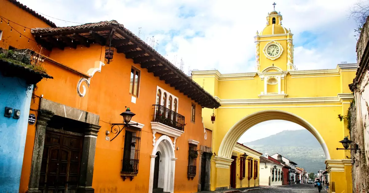 Colorful street with Santa Catalina Arch in Antigua, Guatemala. Vibrant colonial architecture and scenic mountainous backdrop.