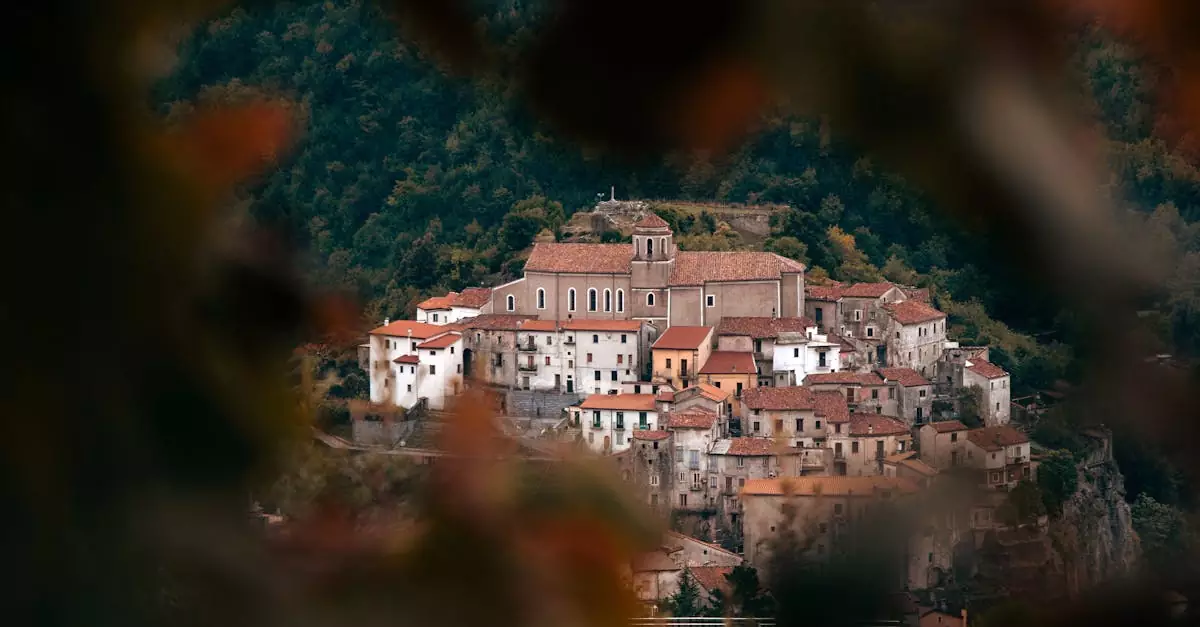 Picturesque view of a rustic Mediterranean village nestled in hills, framed by vibrant autumn foliage.