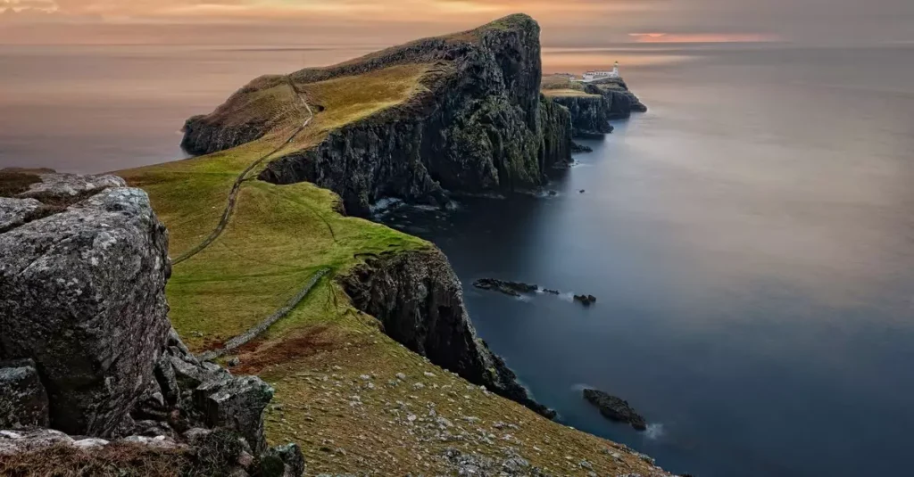A stunning sunset view of Neist Point Lighthouse with cliffs and serene sea in Scotland.