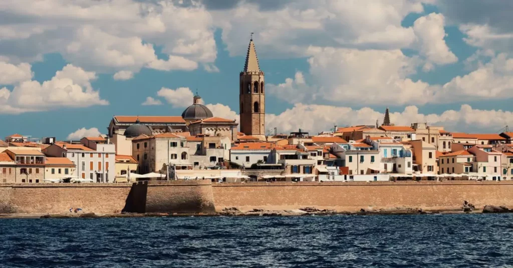 Picturesque view of Alghero's waterfront with historic architecture and vibrant skyline under a clear sky.