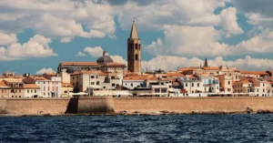 Picturesque view of Alghero's waterfront with historic architecture and vibrant skyline under a clear sky.