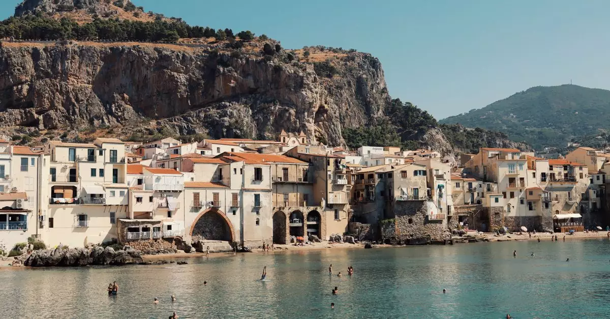 Swimmers enjoy the water with Cefal&ugrave;'s historic seaside buildings and rocky cliffs in Sicily, Italy.