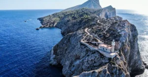 Stunning aerial photo of Punta Grossa Lighthouse on a rocky cliff surrounded by the deep blue ocean.