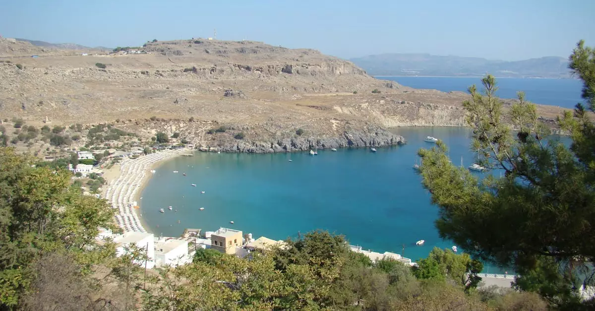 Scenic aerial view of St. Paul's Bay, Lindos, with clear blue waters and surrounding hills.