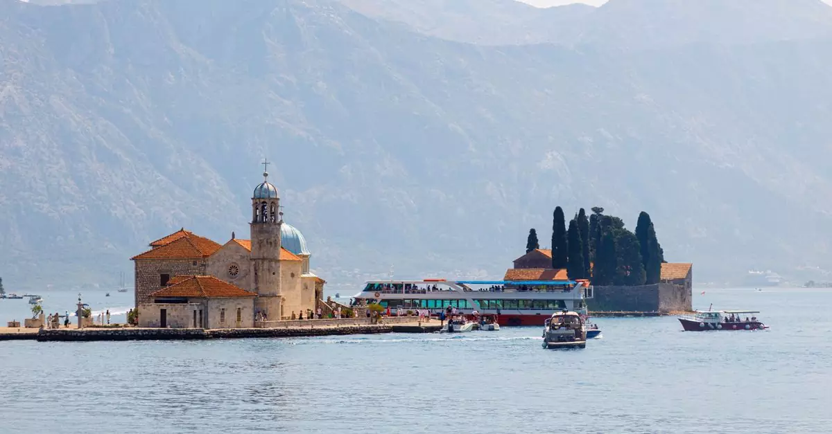 Beautiful shot of Our Lady of the Rocks island in Montenegro's Bay of Kotor with boats and mountains.