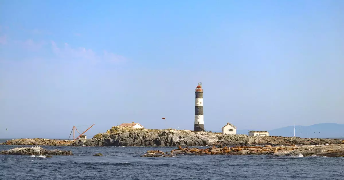Race Rocks Lighthouse stands on a rocky island under a bright blue sky in Metchosin, British Columbia.