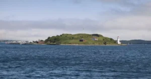 Scenic view of an island with a lighthouse surrounded by blue sea under a partly cloudy sky.