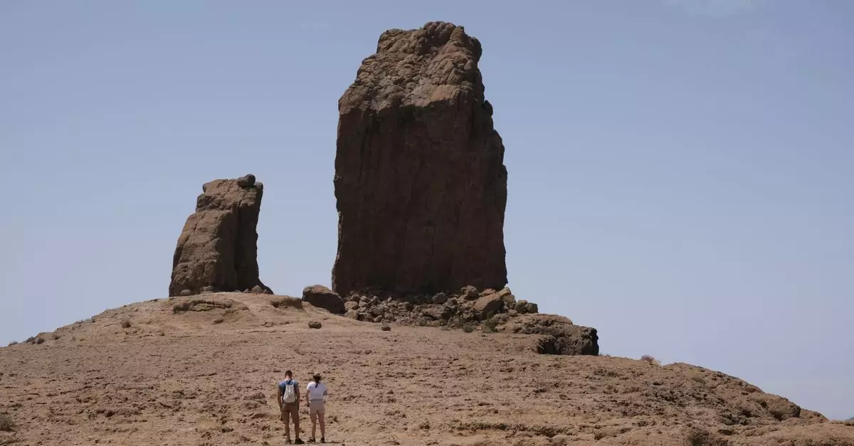 Two hikers explore the iconic Roque Nublo rock formation under clear skies in Gran Canaria, Spain.