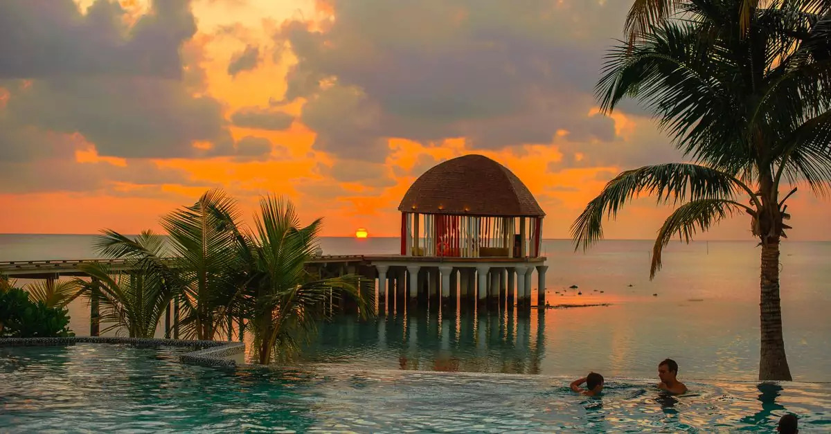 A breathtaking sunset over a tropical Maldives resort with palm trees and ocean views.